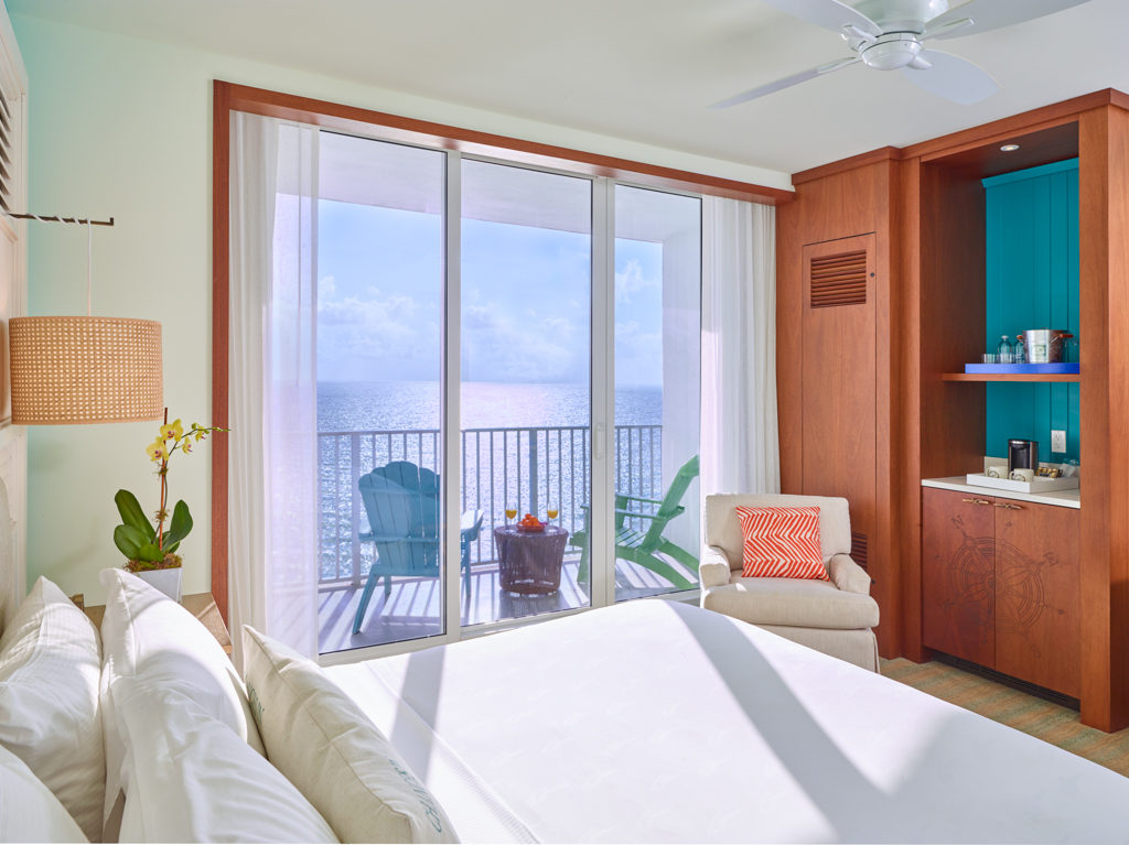 Room with queen bed, armchair, large window and balcony with partial views