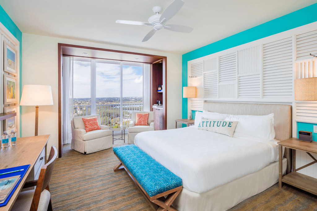 Room contemporary furnishings with a sea and sky color palette and king bed, two armchairs, table and large window