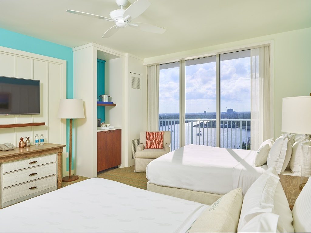 Room contemporary furnishings with a sea and sky color palette and two queen beds, armchair, tv, and large window