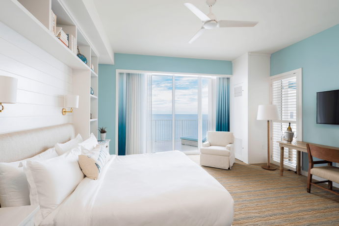 Room contemporary furnishings with a sea and sky color palette, one king bed, armchair, large window and balcony