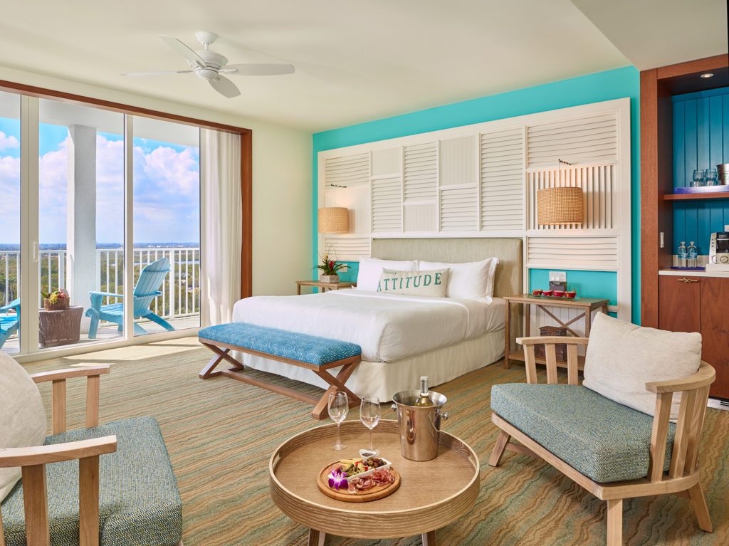 Room contemporary furnishings with a sea and sky color palette, one king bed, armchair, table and two large windows and veranda