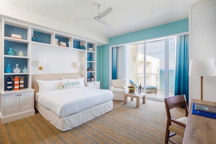 Room contemporary furnishings with a sea and sky color palette, one king bed, armchair, little table, large window and balcony