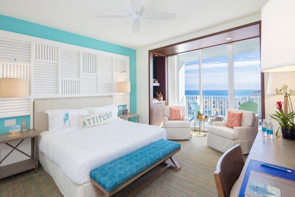 Room contemporary furnishings with a sea and sky color palette and king bed, two armchairs, table and large window