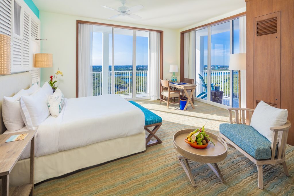 Room contemporary furnishings with a sea and sky color palette, one king bed, armchair, table and two large windows and balcony