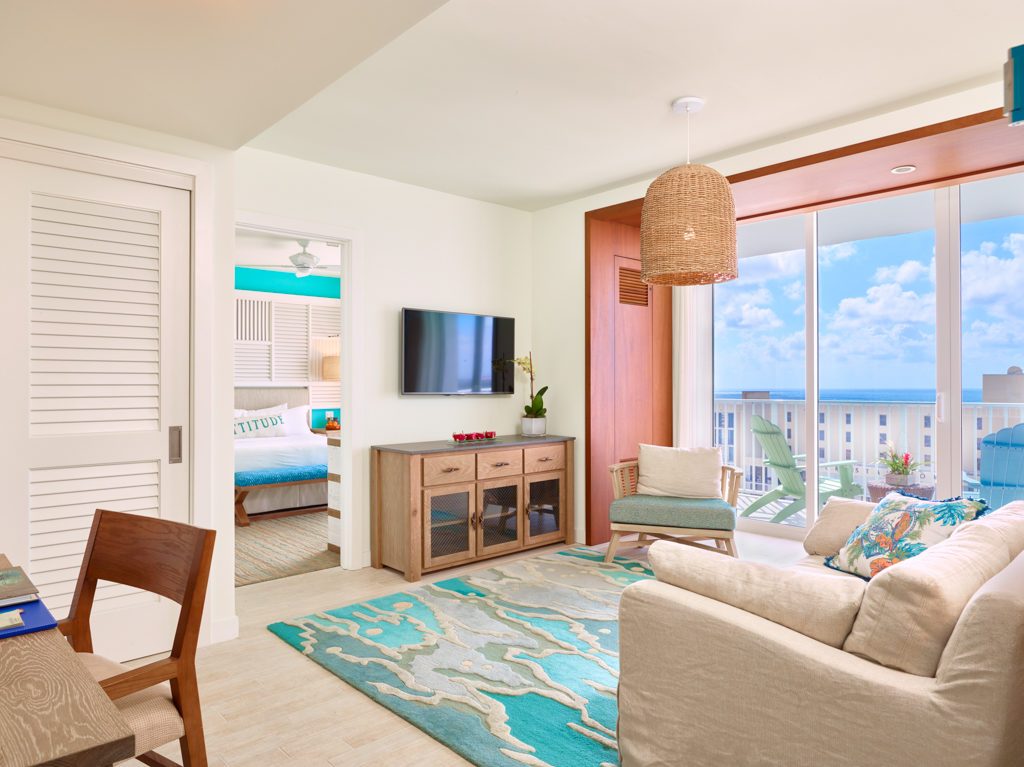 Living room contemporary furnishings with a sea and sky color palette, one sofa, armchair, table, tv, and large window and balcony